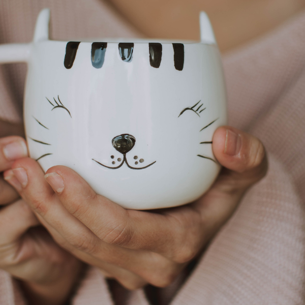 hands holding a mug decorated like a cat face